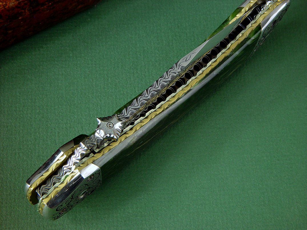 "Procyon" liner lock folding knife, obverse side view,in hand-engraved ATS-34 high molybdenum stainless steel blade, hand-engraved 304 stainless steel bolsters, anodized 6AL4V titanium liners and lockplate, Pounamu New Zealand Greenstone Nephrite Jade gemstone handle, case of Granite, Quartz Terrazzo composite